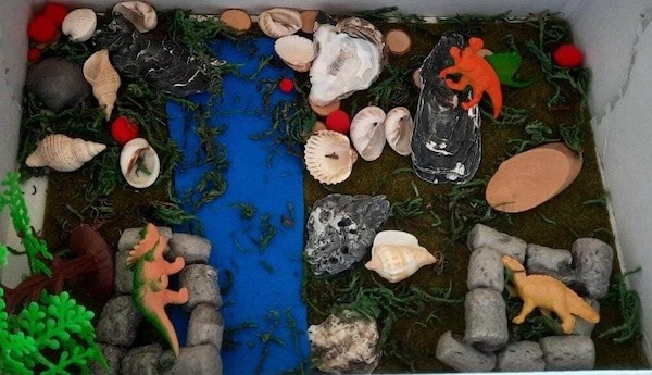 Landschaft in einem Karton, den die Kinder mit Dinos und Bastelmaterial gestaltet haben