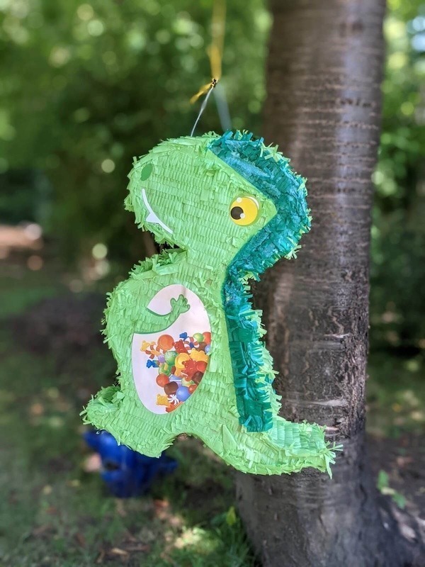 Dino Pinata hängt an einem Baum bei der Dinosaurier Geburtstagsparty
