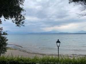 Vom Ufer aus den Gardasee wolkenverhangen mit einer Laterne im Bild