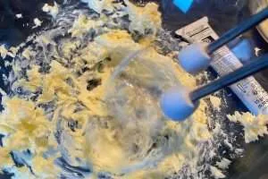 Butter mit Kondensmilch in einer Glasschüssel wird mit den Mixerstäben aufgeschlagen