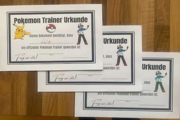 3 Pokemon Trainer Urkunden liegen auf einem Tisch