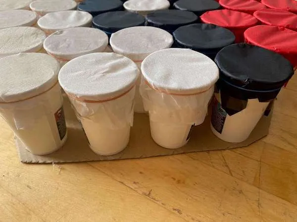 Becher mit einem Seidenpapierdeckel in weiß, schwarz und rot mit einem Gummiband befestigt