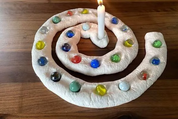 Adventsspirale mit mulden, die alle mit bunten murmeln belegt sind und eine brennende Kerze in der Mitte