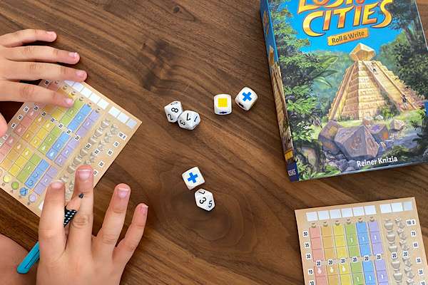 Reisespiel Roll&Write Lost Cities auf dem Tisch aufbereitet mit den 6 Würfeln und den Spielblöcken