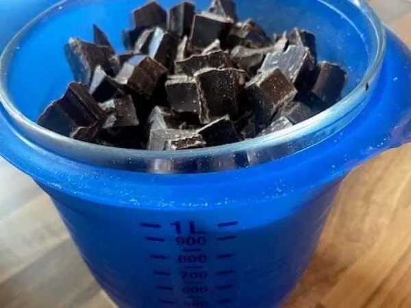 Ein Glas mit dunklen Schokoladenstücken, ideal zum Schmelzen oder Backen, perfekt für Schokoladenliebhaber und süße Rezepte.