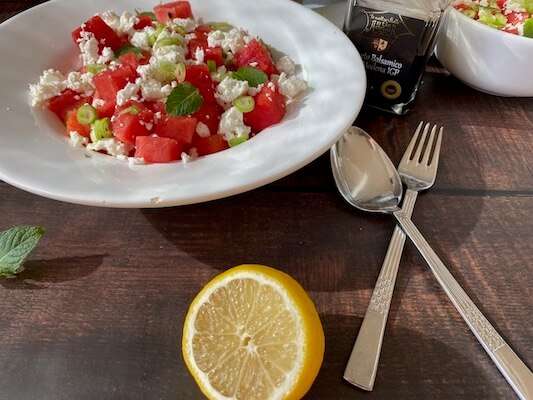 Wassermelonensalat mit Feta  in einem weißen Teller mit einer Zitrone und Besteck