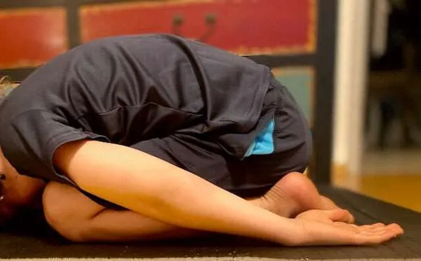 Ein Kind, das am Boden kniet, mit den Händen nach hinten - eine Yoga Übung zur Entspannung