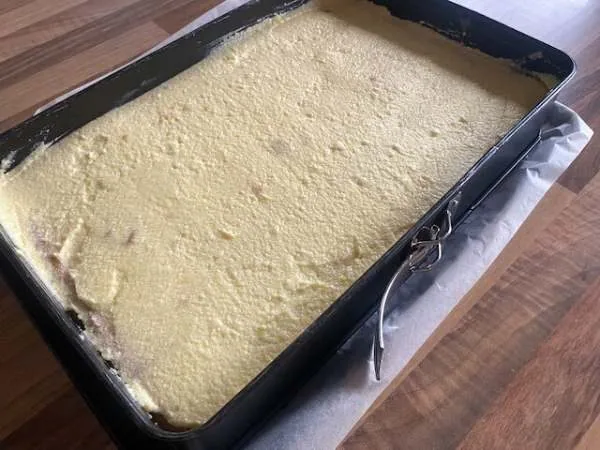 Kuchen in einer rechteckigen Backform vor dem Backen mit Puddingcreme mit einer glatten Oberfläche, auf einer Küchenarbeitsplatte.