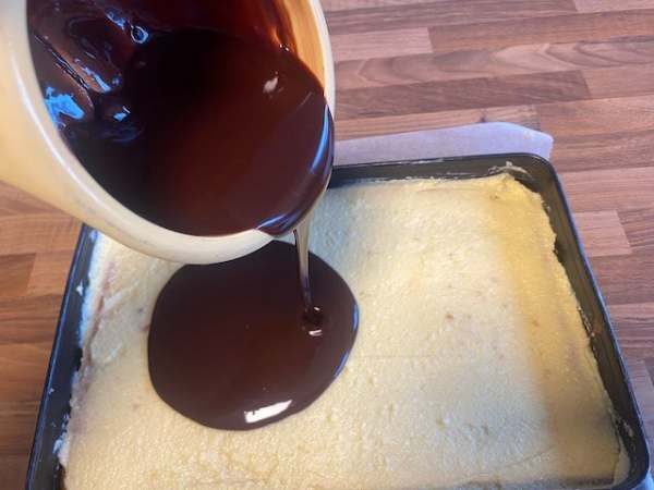 Frisch geschmolzene Schokolade wird gleichm&auml;&szlig;ig auf einen Kuchenteig gegossen, perfekt f&uuml;r Torten und Desserts.