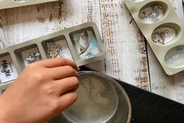 Kinderhand, die flüssiges Glycerin in die einzelnen vorbereiteten Formen mit einem Löffel gießt