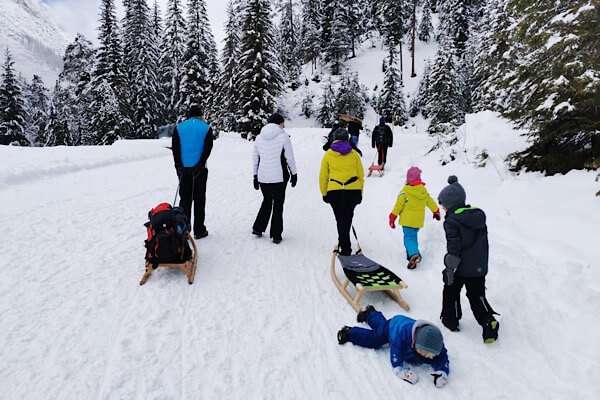 Familiensport im Schnee - einige Erwachsene und Kinder die einen Ausflug mit den Rodeln auf den verschneiten Berg macht