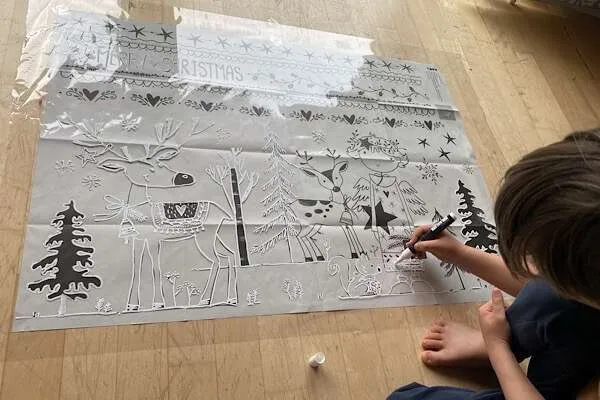 ein Kind, das weihnachtliche Motive von einer Vorlage auf eine Geschenksfolie überträgt