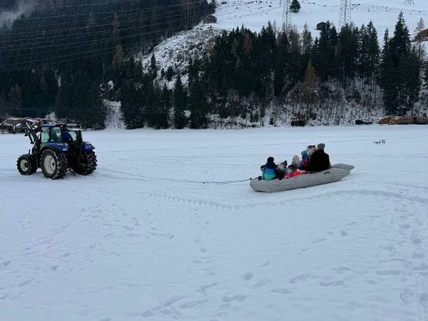 Ein Familienausflug im Winter, bei dem Kinder auf einem Schlitten hinter einem Traktor gezogen werden, in einer verschneiten Berglandschaft, ideal für Familien und Winterabenteuer.