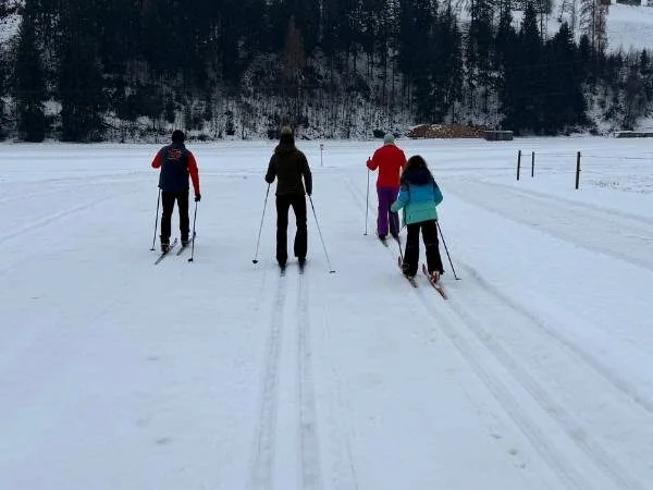 Familie beim Skilanglauf auf einer winterlichen Schneelandschaft, surrounded by Bäume und verschneite Hügel, perfekt für Winteraktivitäten mit Kindern und Freunden.