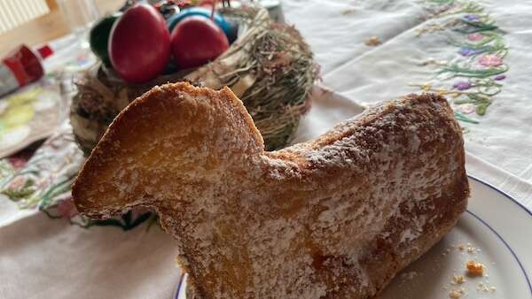 Osterlamm aus Biskuit im Vordergrund, Ostereierkorb im Hintergrund auf einem Tisch 