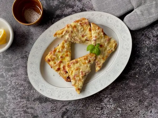 Flammkuchentoasts in Dreiecke geschrieben auf einem ovalen weißen Teller