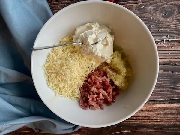 Zutaten des Flammkuchen-Toasts in einer weißen Schüssel: Zwiebel, Käse, Speck, Creme fraiche