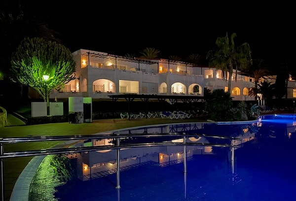 Elegantes Hotel am Pool bei Nacht auf Fuerteventura, ideal f&uuml;r Familienurlaub mit Kindern, entspannte Atmosph&auml;re, moderne Architektur, tropische Pflanzen, beleuchteter Au&szlig;enbereich, Urlaubsstimmung.