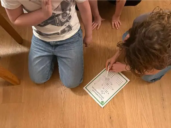 Ein Kind zeichnet auf einem Countdown-Board, um die Tage bis Silvester zu zählen, während ein anderes Kind daneben sitzt und zuschaut.