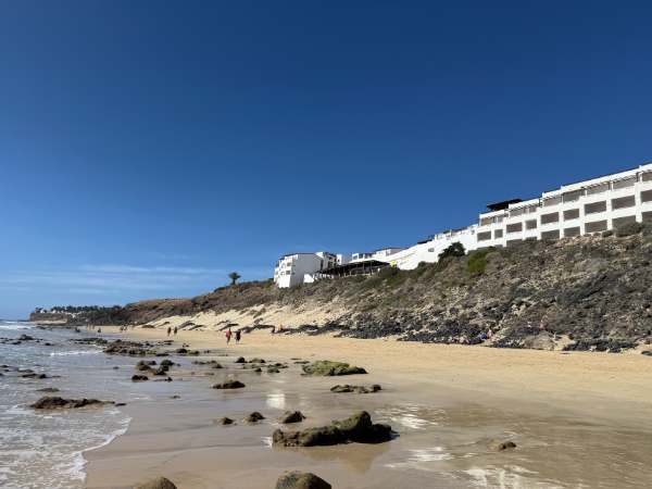 Familienurlaub auf Fuerteventura mit Kindern am Strand, Sand, Felsen und Hotel im Hintergrund, ideal f&uuml;r einen entspannten Familienurlaub mit Kindern.