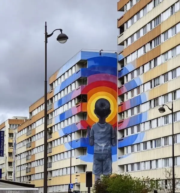 Grafitti an einer Häuserwand in paris mit einem Kind und drum herum ein Regenbogen