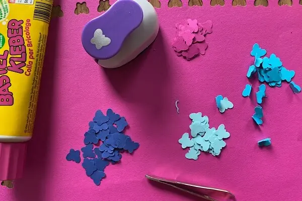 Schmetterlingsstanzer, Papier und Kleber und Pinzette auf einem rosaroten Papier