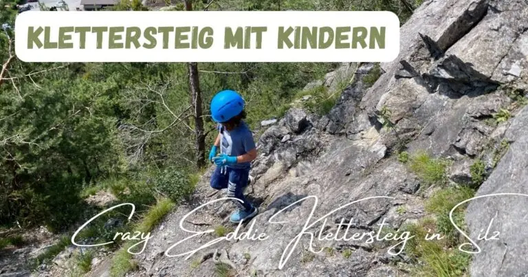 Beitragsbild mit dem Titel Klettersteig mit Kindern und einem Kind, das gerade mit Helm den Klettersteig hinunter geht im Hintergrund