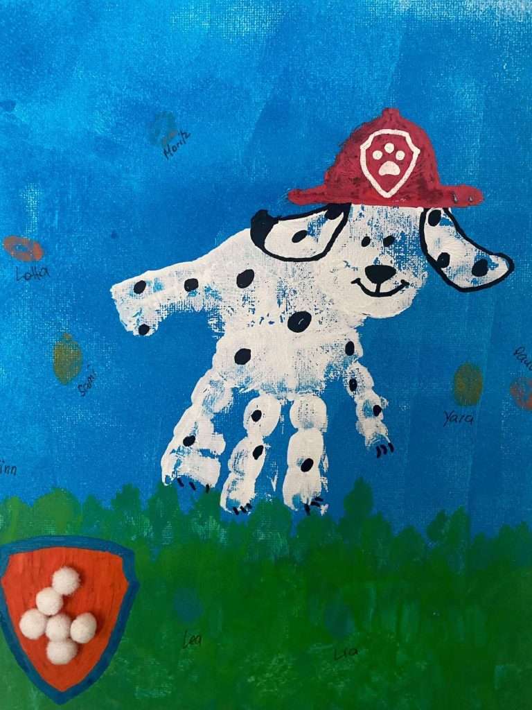 Bild mit einem weißen Handabdruck, der zu einem Paw Patrol Hund gestaltet wurde. Mit Fingerabdrücken der Gästekinder