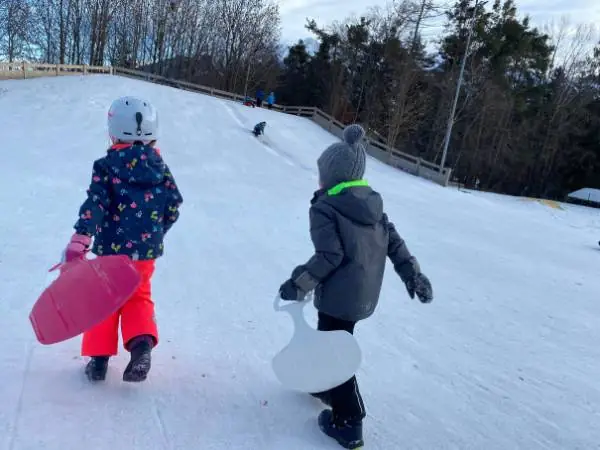2 Kinder auf dem Weg einen Rodelhügel hinauf