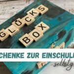 Glücksbox mit den Holzbuchstaben Glücksbox und dem Titeltext "diy geschenke zur einschulung selbstgemacht"