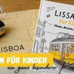Lissabon Reiseführer für Kinder mit Mal und Rätselaufgaben liegt auf einem Tisch, daneben eine kleine Tram 28 und der Schriftzug Lisboa