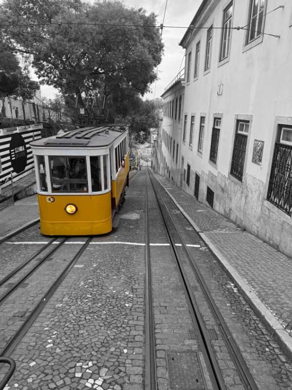 Ascensor da Gloria in Lissabon, wie sie den Berg hoch fährt in schwarz-weiß - nur die Bahn ist gelbe