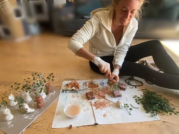 Ich sitze am Boden und gestalte die Alraunen als Einladung für den Zauberer Geburtstag mit Unterlage und Pflanzenteilen und mit Handschuhen
