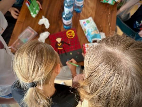 Kinder stehen an einem Tisch und schreiben ihren Namen auf das Fingerabdruckbild