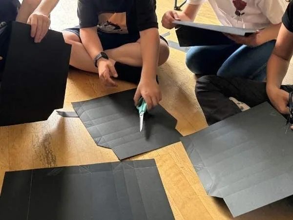 Kinder haben schwarzes Papier mit geritten Linien zum Ausschneiden und falten in den Händen