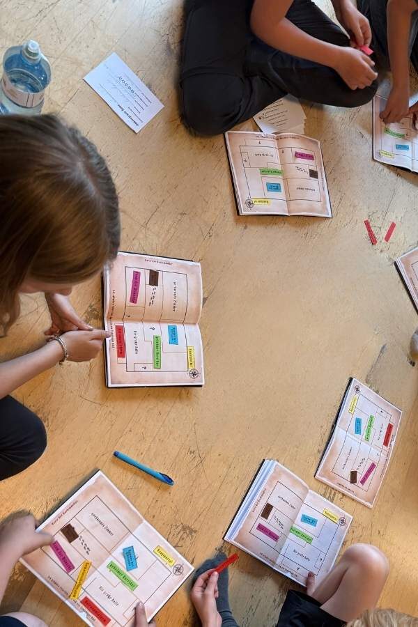 Kinder sitzen am Boden und füllen die Prüfungsbücher mit bunten Kärtchen aus