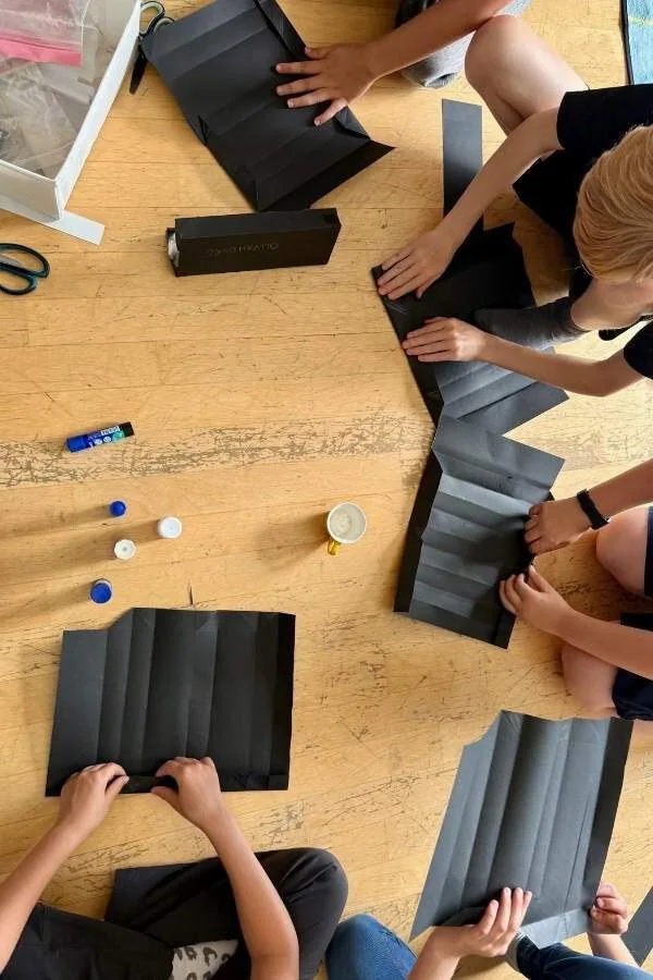 Bilder von Kindern, die schwarze Bastel- oder Bastelkartonarbeiten auf einem Holztisch durchführen, gemeinsam kreativ tätig.