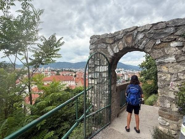 Kind steht in einem steinernen Durchgang, im Hintergrund die Häuser von Graz