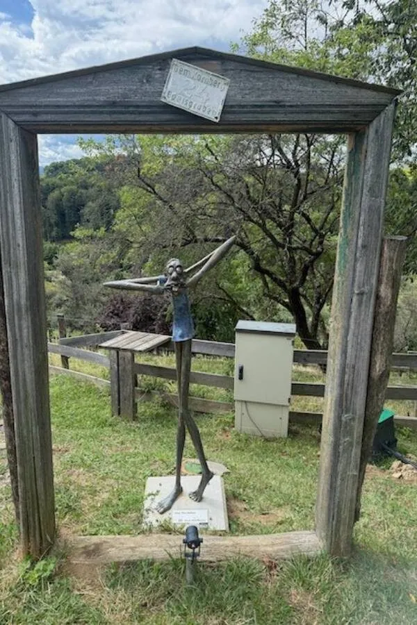 Schaukelnde skulptur im freien, kunst im park mit baum und felsen im hintergrund, moderne metallskulptur eines tanzenden menschen, outdoor kunstinstallation, kreative skulptur für öffentliches raumdesign, MamaBlog.
