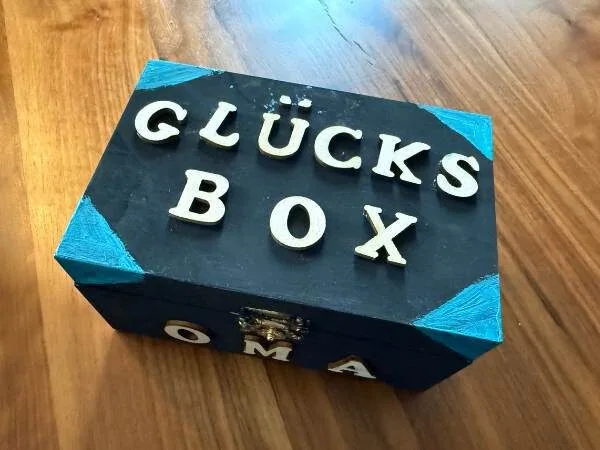Box mit Holzbuchstaben mit dem Text Glücksbox auf einem Tisch liegend