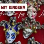 Venezianische Masken auf rotem Hintergrund mit dem Titel: Venedig mit Kindern - Unser toller Tag in der Lagunenstadt