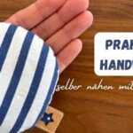eine Hand mit einem kleinen Handwärmer blau weiß gestreift mit dem Titel: praktische handwärmer selber nähen mit Kindern