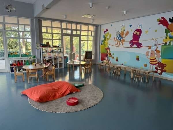 Kinderclub mit einem Teppich in der Mitte und vielen Tischen und Stühlen