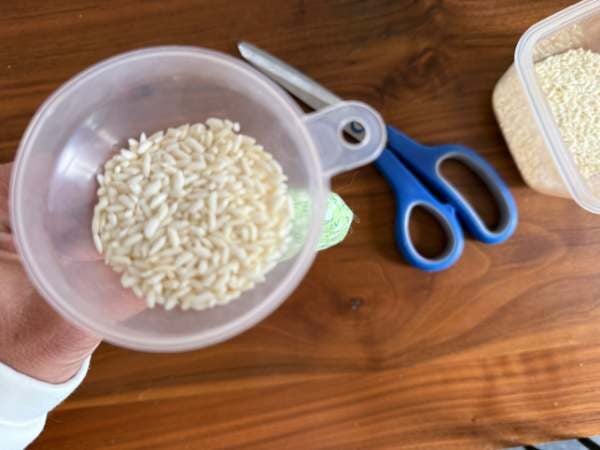 Eine Hand die einen Trichter hält, der mit Milchreis gefüllt ist, daneben Schere und restlicher Milchreis