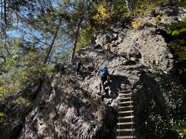 Kletterer auf steiler Felswand im Wald, Abenteuer und Naturerlebnis in den Bergen, Outdoorsport für Mutige, Waldpfad mit Klettersteig.