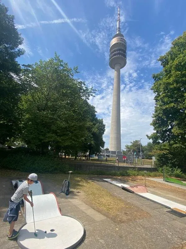 Olympiaturm im Hintergrund und ein Kind, das Minigolf spielt im Vordergrund