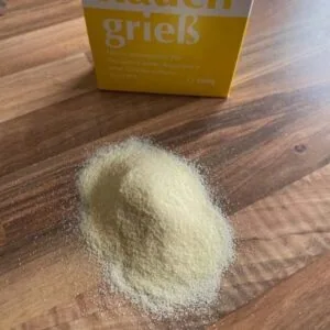 Grieß auf einer HOlzarbeitsplatte dahinter steht die Grießpackung in gelb