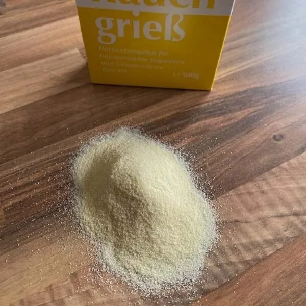 Grieß auf einer HOlzarbeitsplatte dahinter steht die Grießpackung in gelb