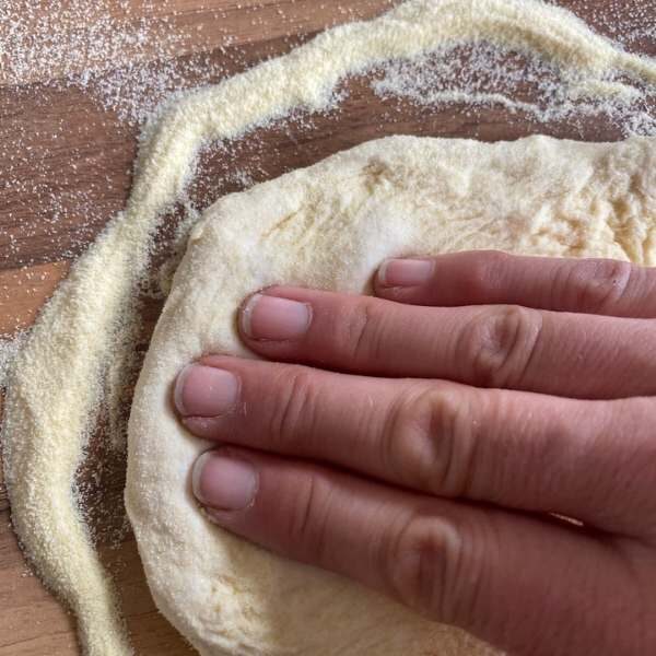 Finger, die einen Pizzateig am Grießbett auseinander drücken
