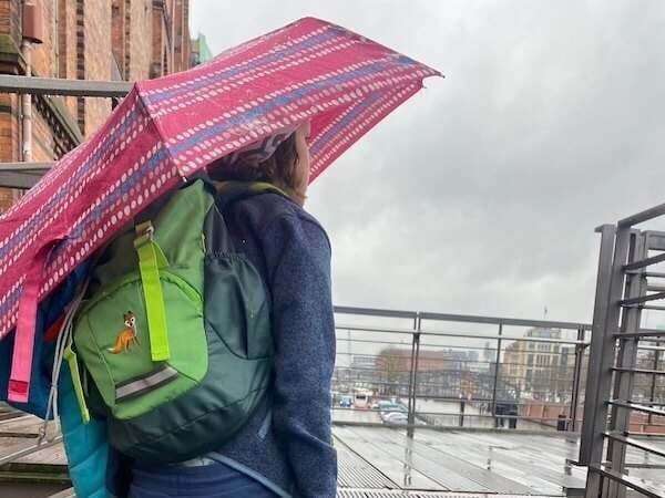 Kind Regenschirm und Rucksack bei Regenwetter in Stadt.